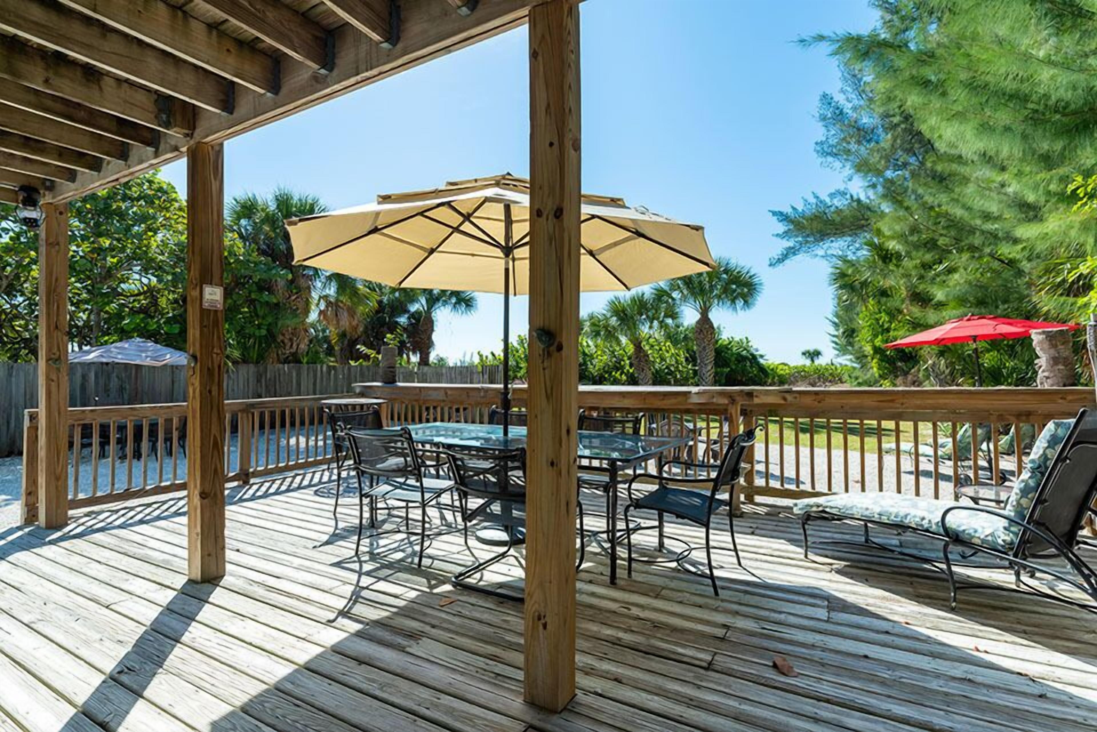 A wooden deck with a glass table and chairs, a red umbrella, and a wooden pergola.