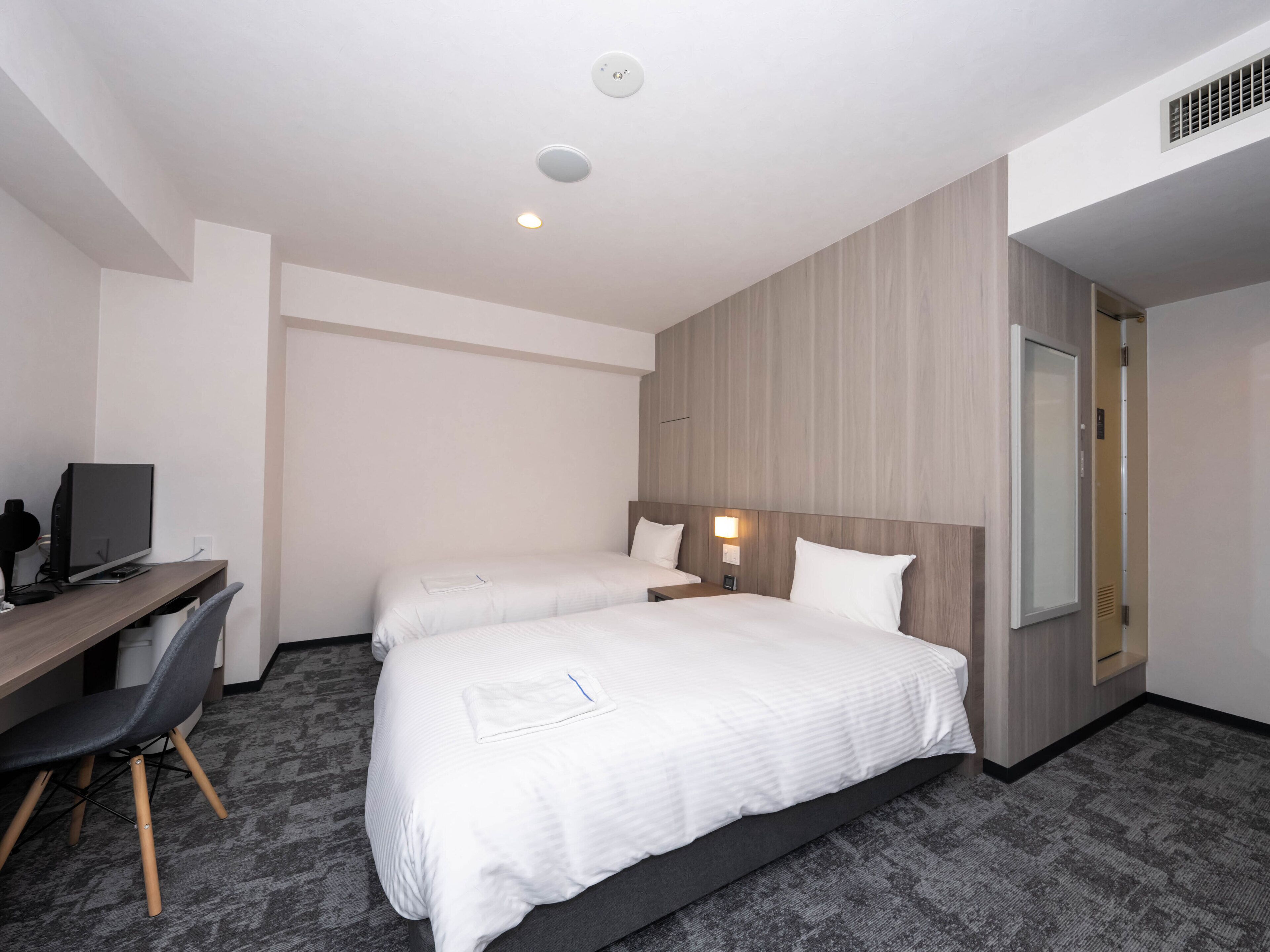 A hotel room with two beds, a desk with a computer, and a large mirror.