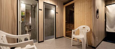 A modern spa room with wooden paneling, a glass shower enclosure, and two white plastic chairs.