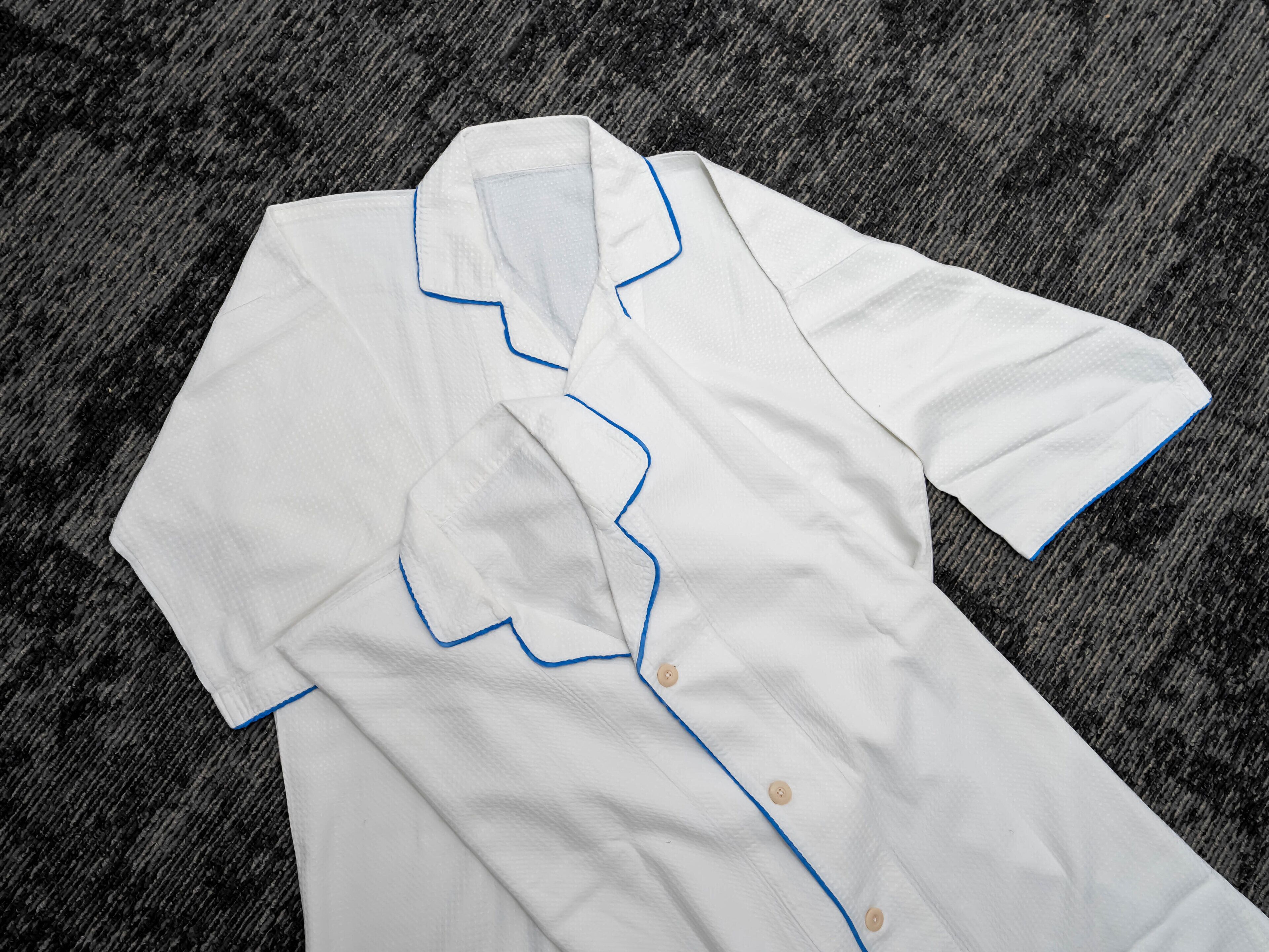 A white shirt with blue trim and buttons laid on a textured surface.