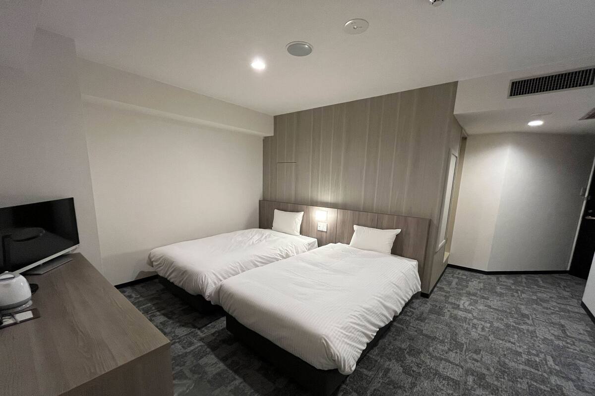 Une chambre d’hôtel avec deux lits, un bureau doté d’un téléviseur à écran plat et une armoire intégrée.