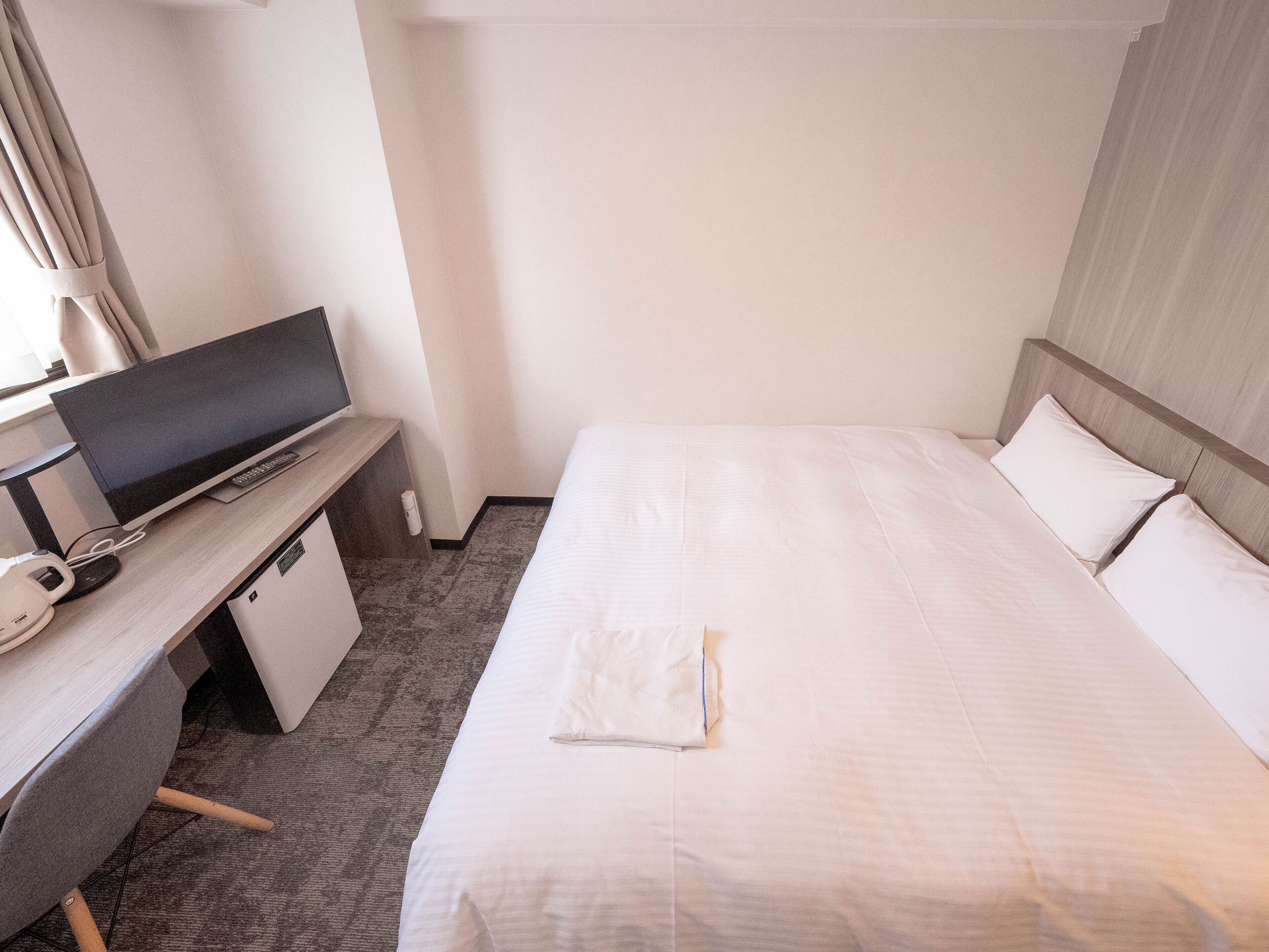 Una habitación de hotel con cama, escritorio con computadora y ventana con cortinas.