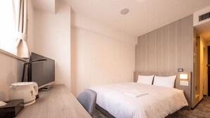 A hotel room with a bed, a desk with a computer and a coffee maker, a TV, and a wall-mounted light. - GARDENS STAY (Sapporo)
