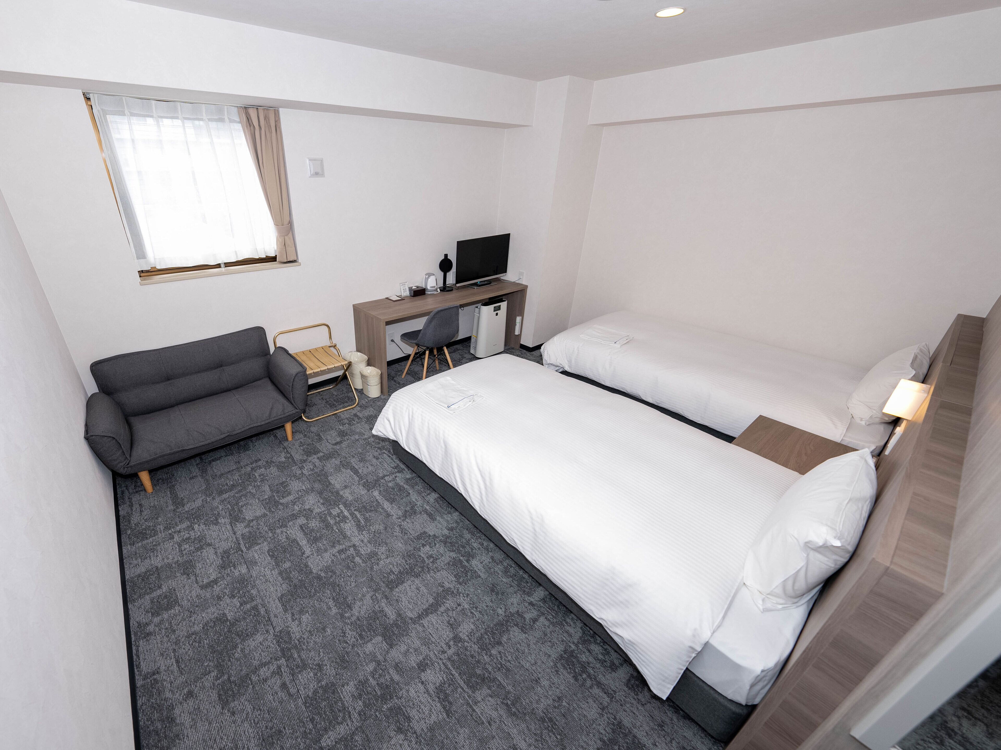 Ein Hotelzimmer mit zwei Betten, einem Schreibtisch, einem Sessel, einer Couch und einem Fernseher.