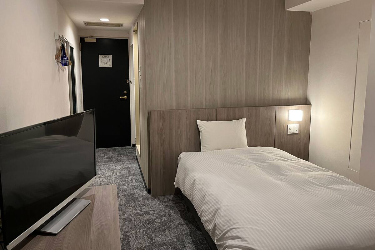 Une chambre d’hôtel équipée d’un lit, d’un téléviseur à écran plat, d’une tête de lit en bois et d’une lampe fixée au mur.