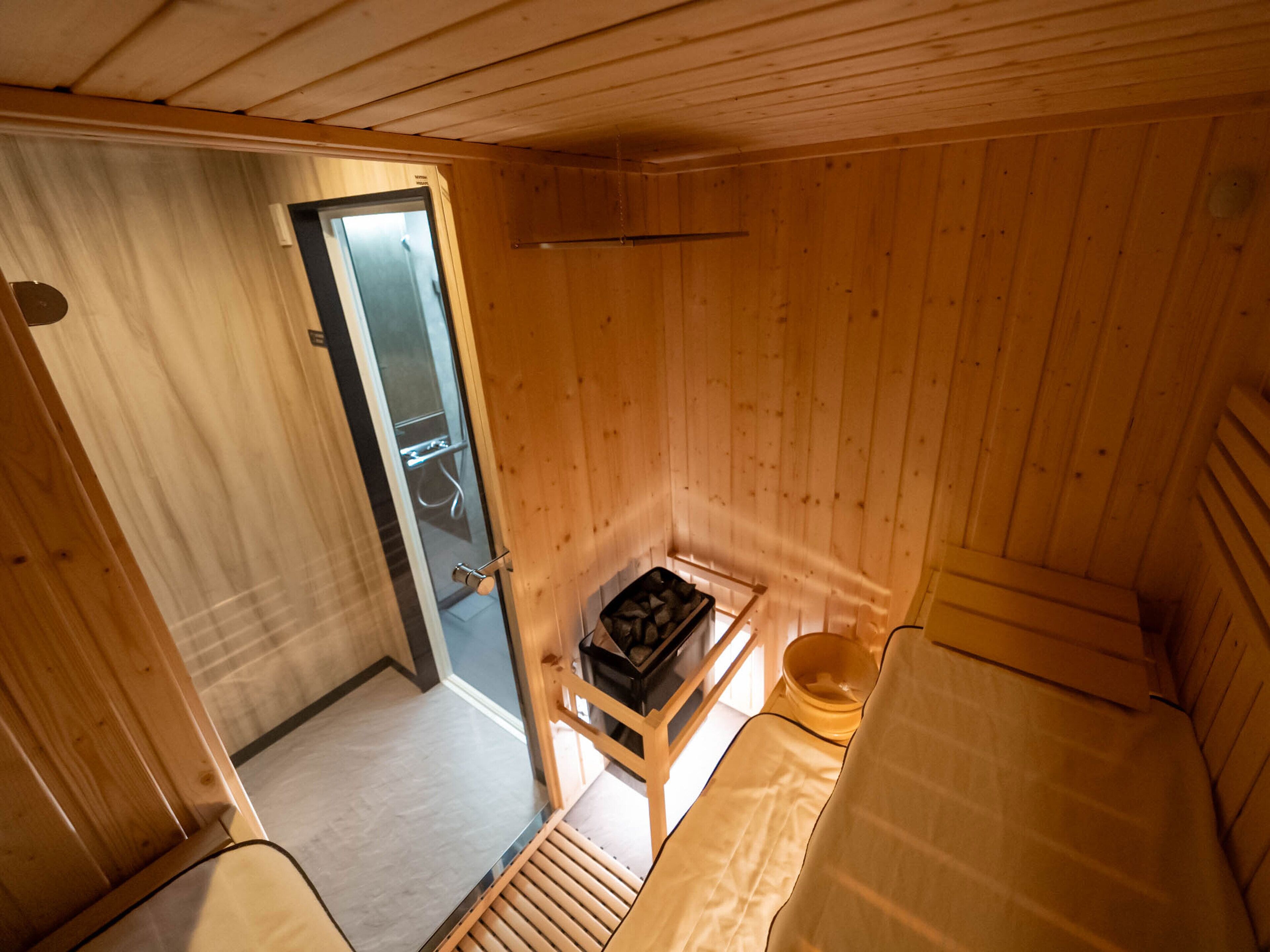Una pequeña cabaña de madera con una sola puerta que da a un baño, una mesita con una silla y un banco.