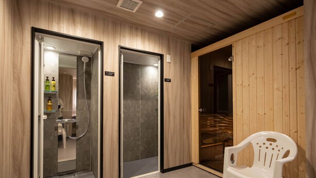 A hotel bathroom with wooden paneling, a shower area, and a white plastic chair. - GARDENS STAY (Sapporo)