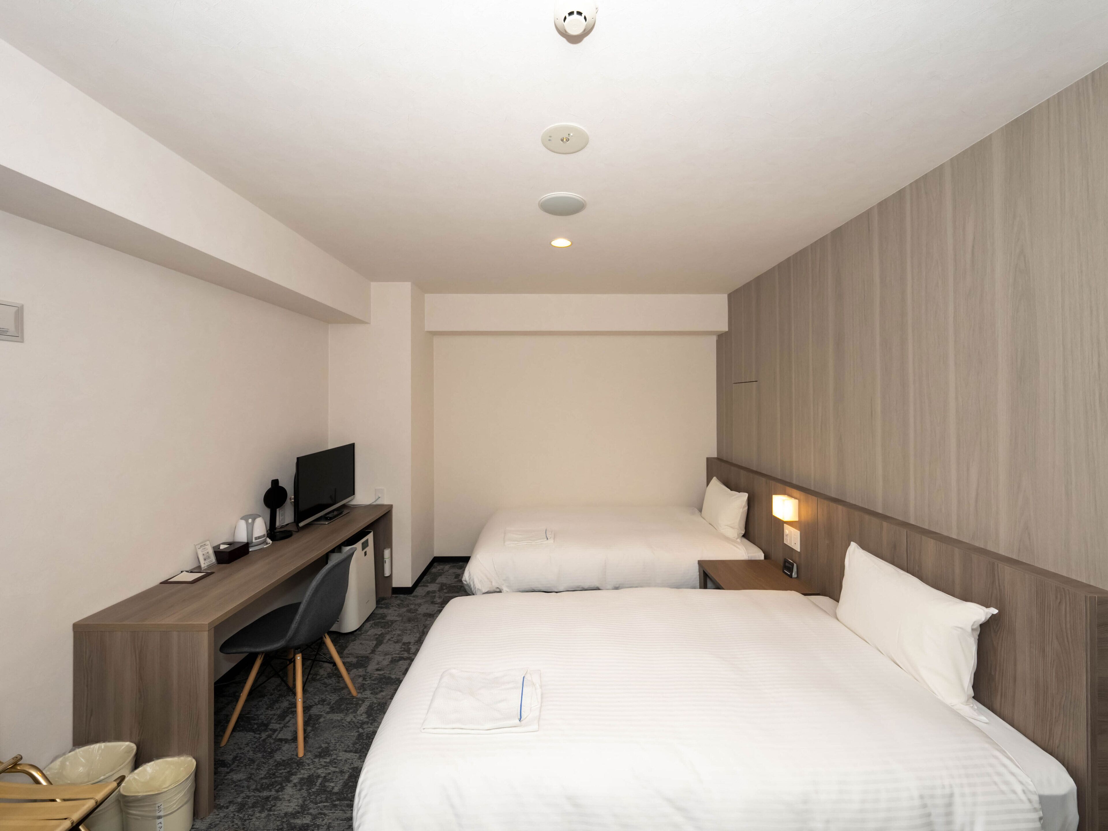 A hotel room with two beds, a desk with a TV, and a small seating area.