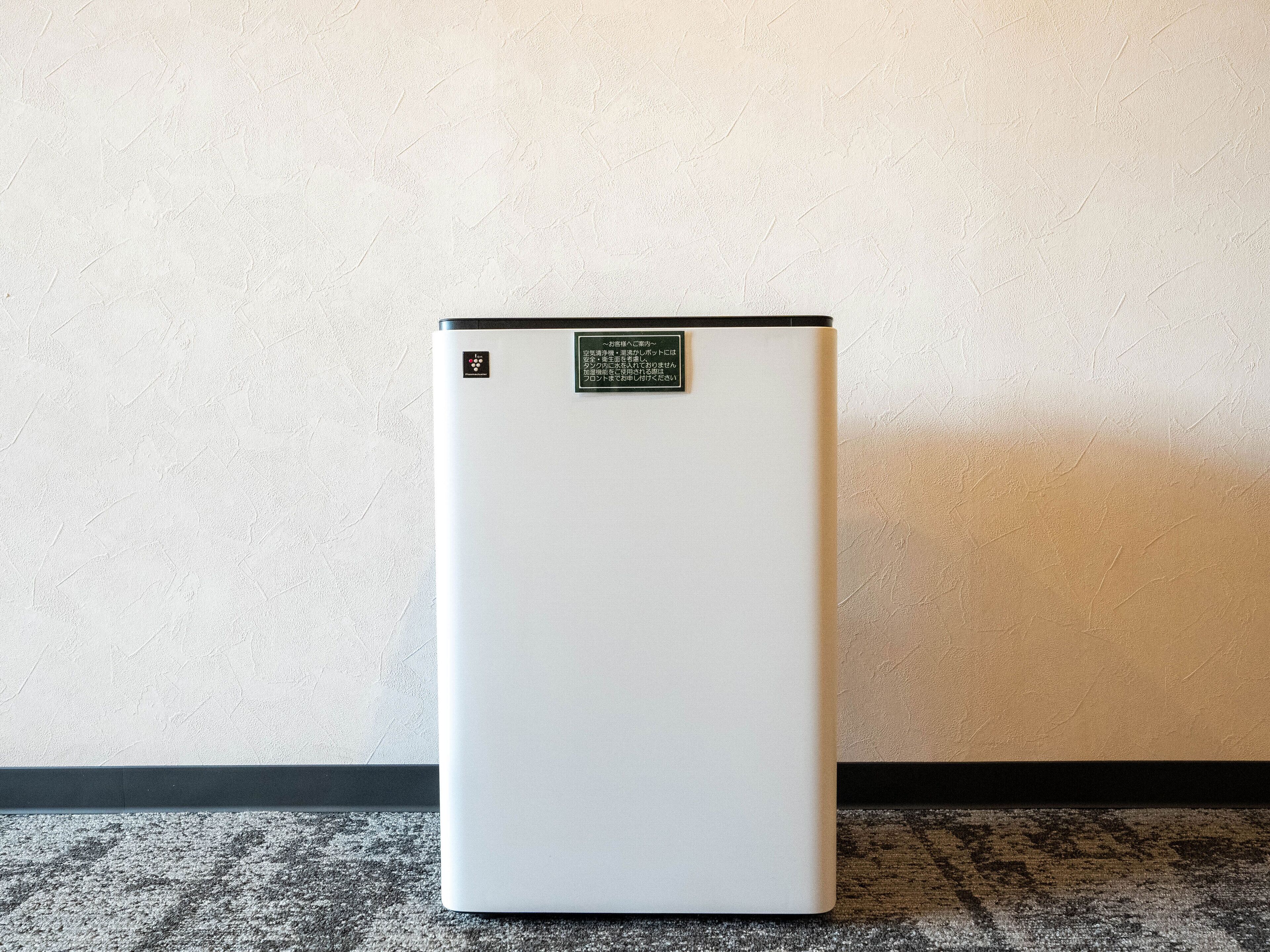 A white portable heater with a control panel and a warning label, placed against a textured wall.