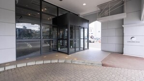 A modern building entrance with glass doors, a tiled pavement, and a sign reading "GARDENS STAY". - GARDENS STAY (Sapporo)