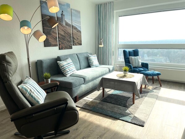 A modern living room with a sofa, armchair, coffee table, and a view of the city through a large window.
