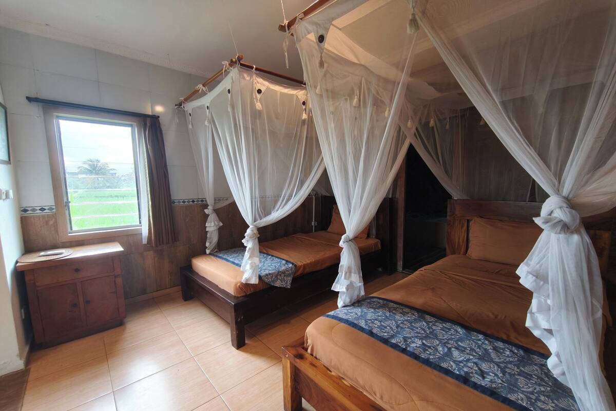 Una habitación con dos camas, cada una con dosel, un armario de madera y una ventana con vistas a la vegetación.