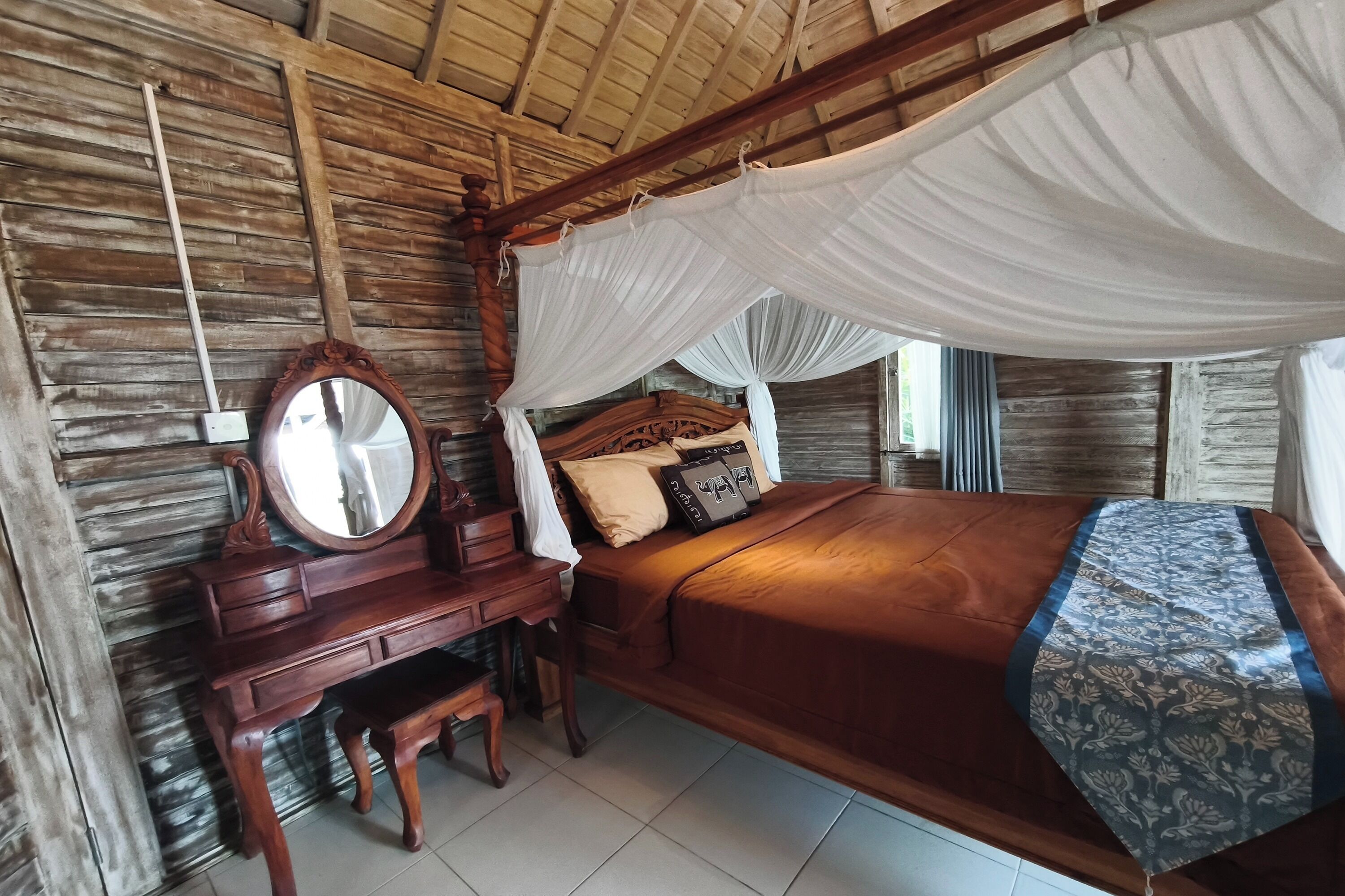 A wooden bed with a canopy, a wooden dresser, and a mirror.