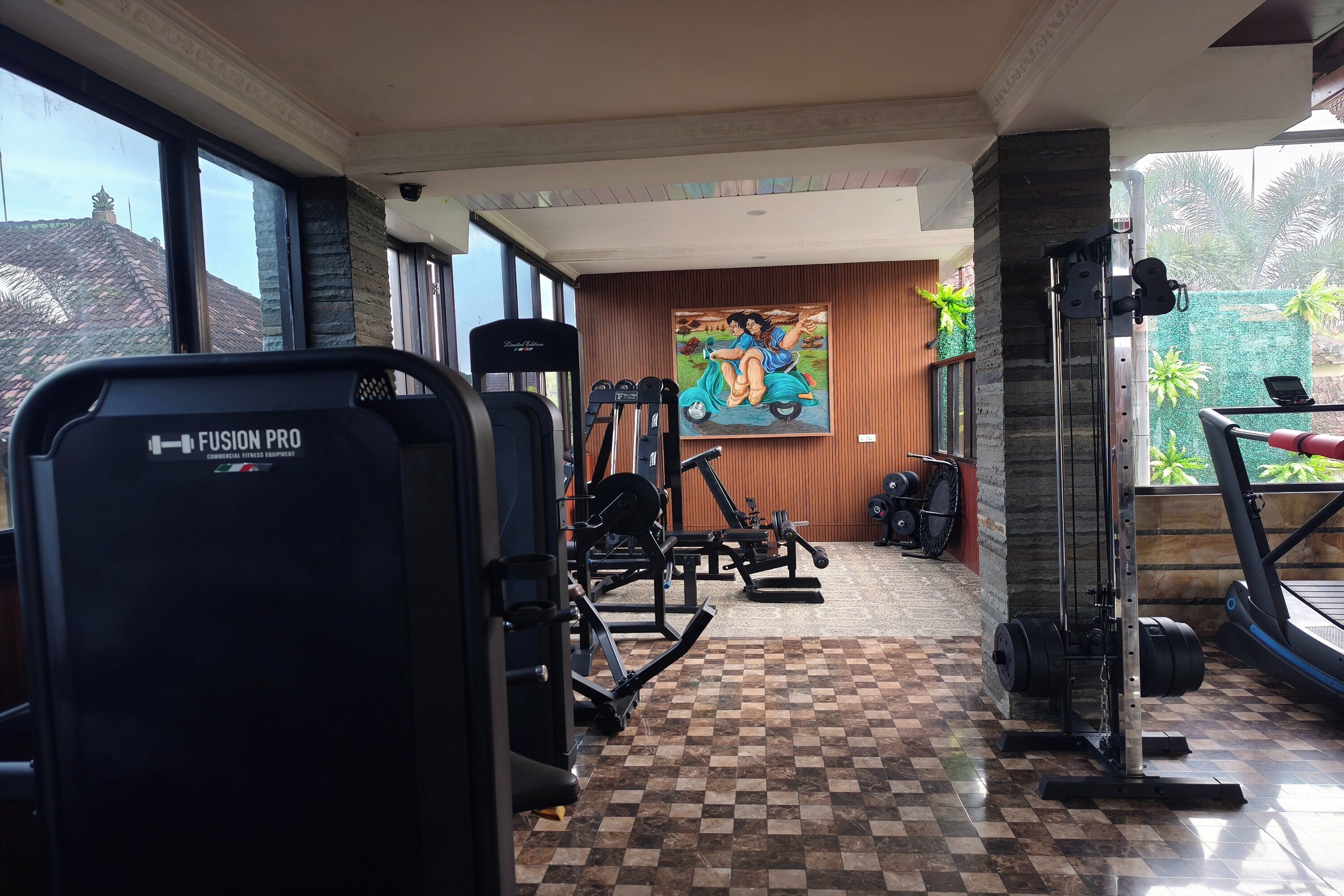 A gym with various exercise equipment, a checkered floor, and a mural on the wall.