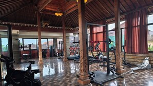 Un gimnasio con equipo de ejercicio, pilares de madera y ventanas amplias.