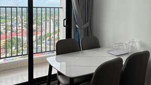 A modern hotel room with a large window, a dining table with chairs, and a balcony with a view of the city. - Tecco Elite Serviced Apartments (Quyet Thang)