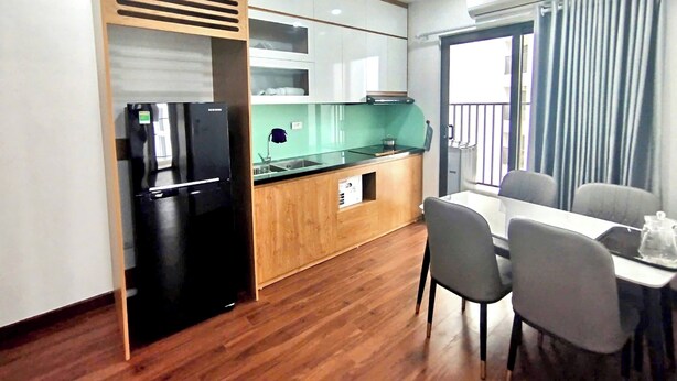 A compact kitchen with a black refrigerator, wooden cabinets, a sink, and a dining area with a table and chairs. - Tecco Elite Serviced Apartments (Quyet Thang)