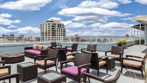 Una terraza en la azotea con mobiliario de mimbre, una piscina y vistas del horizonte de la ciudad.