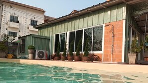 A swimming pool with clear water, a building with large windows, and potted plants along the side.