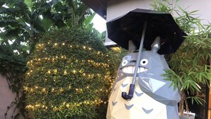 A geometric sculpture resembling a character with a black umbrella, placed outdoors near a hedge with string lights. - Casa Coco Hotel (Nakhon Ratchasima)