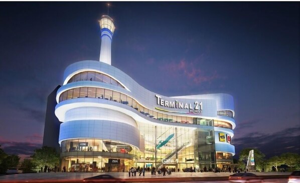 A modern building with a curved facade, labeled "Terminal 21 KORAT," featuring multiple levels, large glass windows, and a prominent tower. - Casa Coco Hotel (Nakhon Ratchasima)
