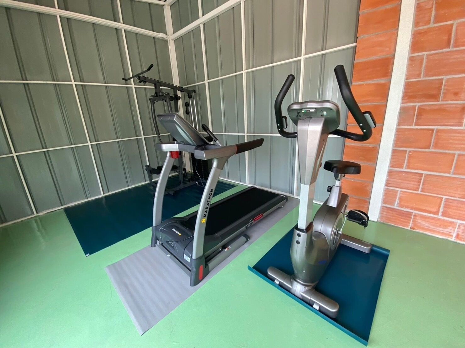 A gym with a treadmill, elliptical, and stationary bike on green mats.