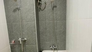 A bathroom with a white bathtub, grey tiled walls, and a wooden floor.
