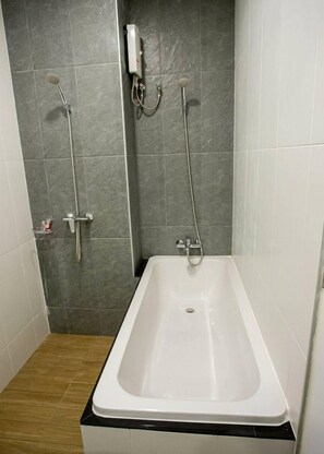 A bathroom with a white bathtub, grey tiled walls, and a wooden floor.