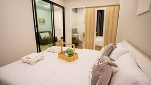 A hotel room with a bed, a wooden side table with a basket, a plush toy, and a mirror. - Casa Coco Hotel (Nakhon Ratchasima)