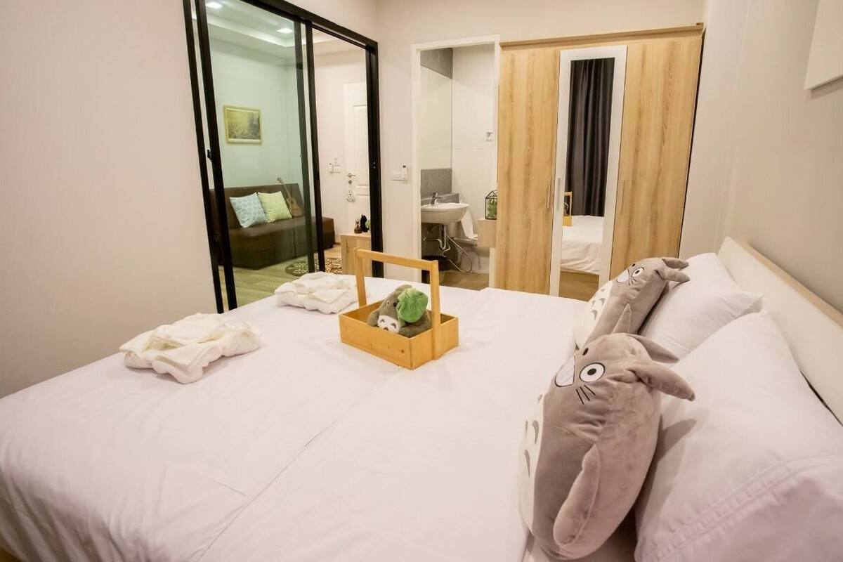 Una habitación de hotel con una cama, una mesita de madera con una cesta, un peluche y un espejo.