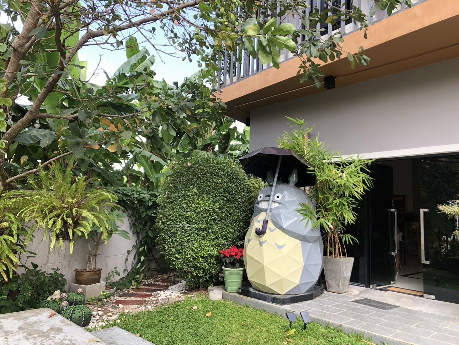 Un jardin agrémenté d’une grande sculpture décorative, d’une plante en pot et de l’entrée d’un bâtiment.