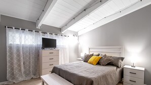 Ein Schlafzimmer mit Bett, Nachttisch, Bank und einem Fernseher auf einem Schrank.