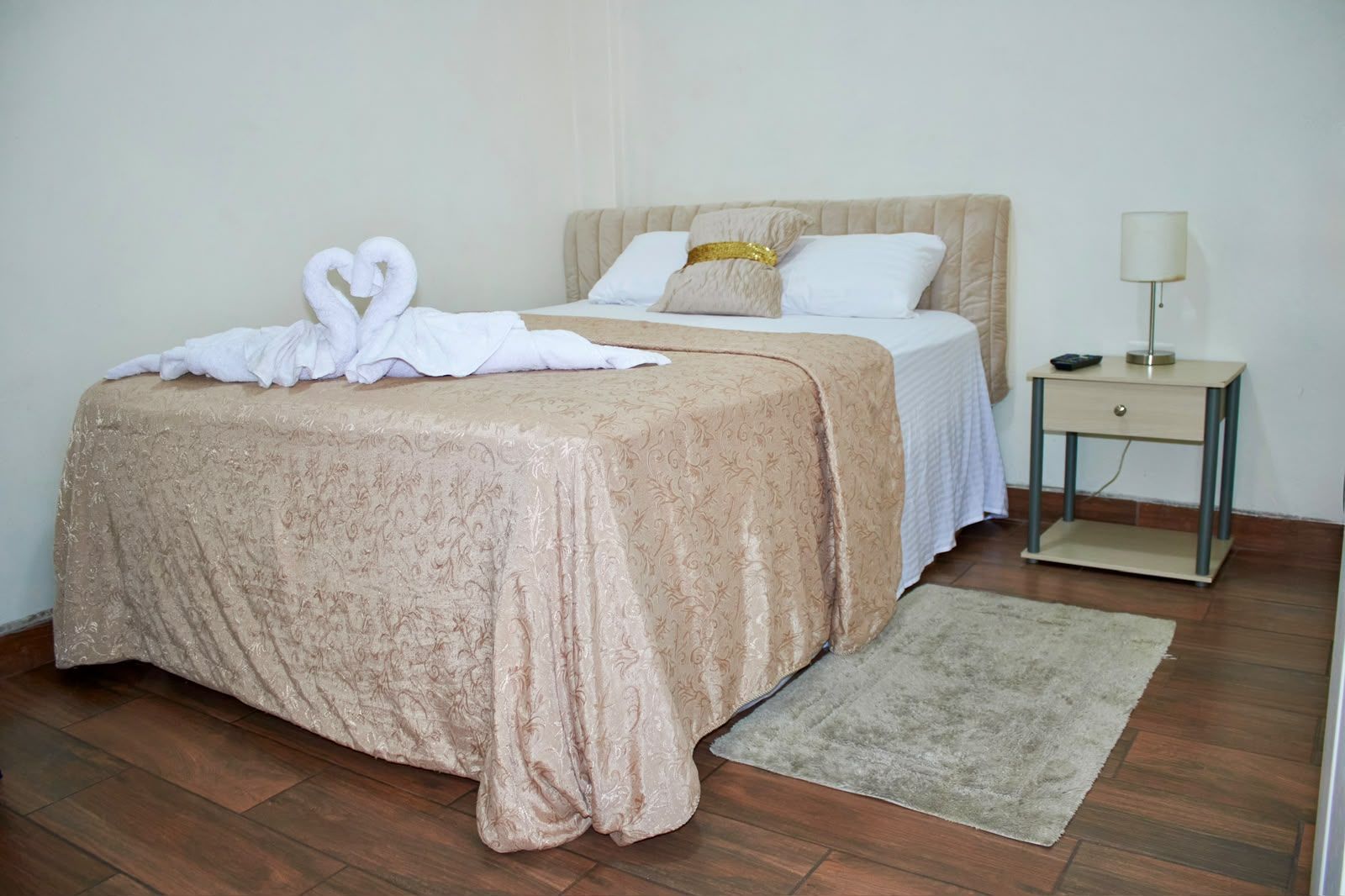 A neatly made bed with a decorative headboard, a bedside table with a lamp, and a rug on a wooden floor.