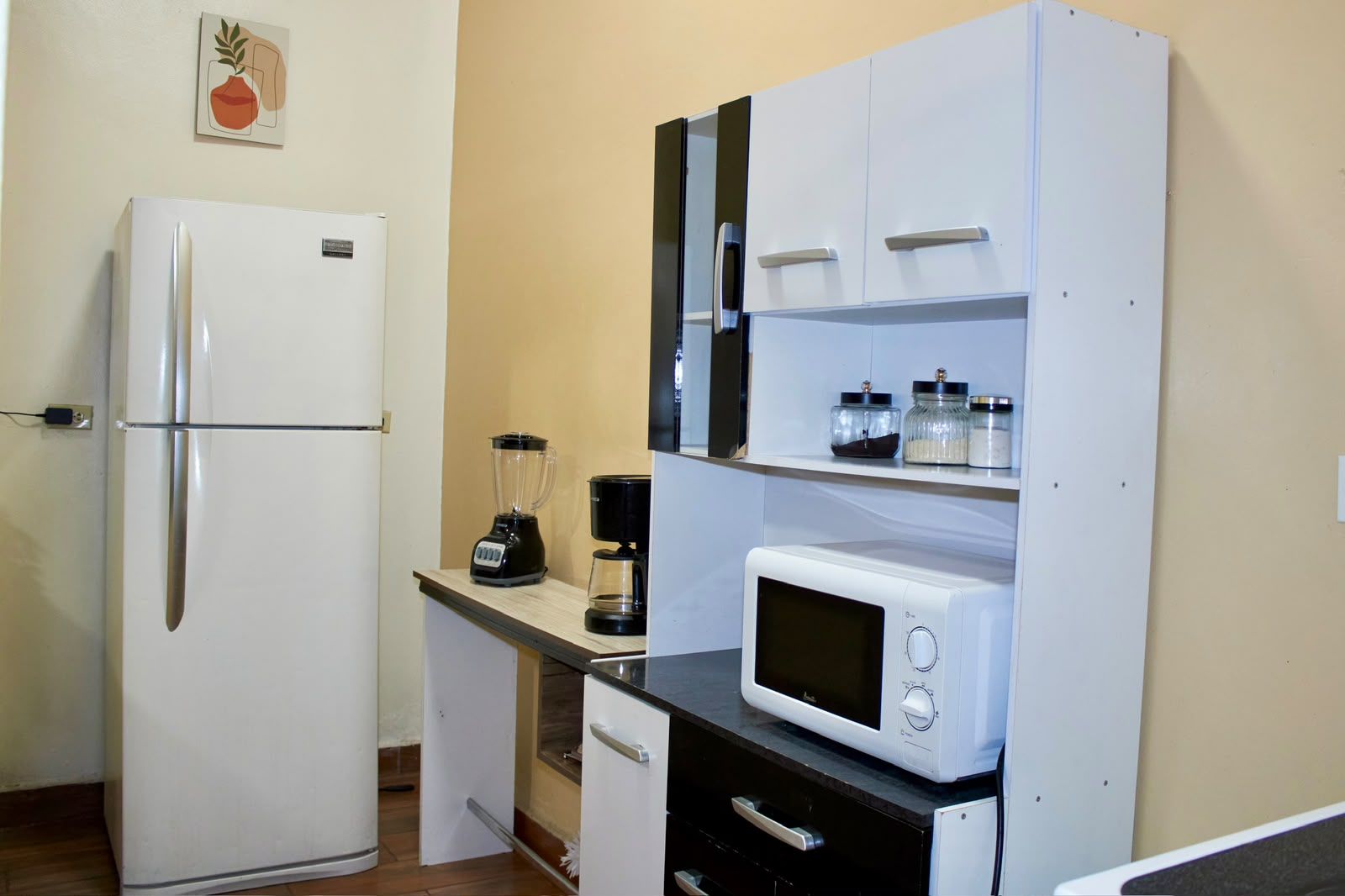 A compact kitchen with a refrigerator, a microwave, a blender, and a coffee maker.