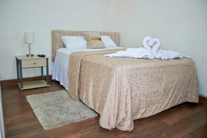 Quarto bem arrumado com cama, mesa de cabeceira, abajur e uma toalha decorativa em formato de cisne sobre a cama.