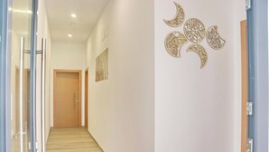 A hallway with a wooden door at the end, a wall-mounted artwork, and a decorative wall piece with crescent shapes. - La Ilusión, studio in Conil de la Fra. (Conil de la FRa.)