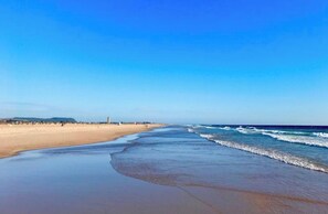 Ein weiter Sandstrand mit sanften Wellen und blauem Himmel.