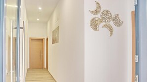 En hall med en trädörr längst in, ett konstverk som hänger på väggen och en dekorativ väggpanel med halvmåneformade detaljer.
