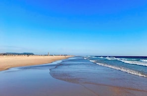 Uma praia extensa com ondas suaves e céu claro.