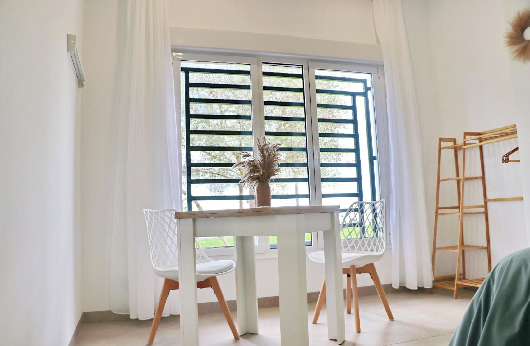 A room with a table and chairs, a window with blinds, a ladder, and a potted plant.
