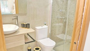 A modern bathroom with a glass shower enclosure, a white toilet, and a sink with a mirror above it. - La Ilusión IV, studio in Conil. (Conil de la Fra.)