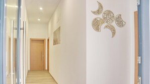 A hallway with a wooden door at the end, a glass door on the left, and a wall with decorative moon cutouts. - La Ilusión IV, studio in Conil. (Conil de la Fra.)