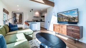 A modern living room with a green sofa, a black ottoman, and a wooden cabinet with a TV mounted above. - Sweet 1Bed/Loft/1Bath EagleVail (Avon)