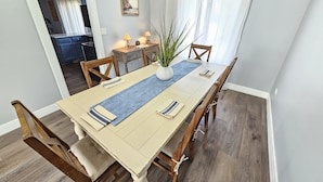 Et spiseområde med et langt bord, træstole, en vase med en plante og et maleri på væggen.