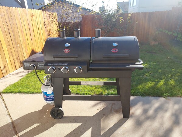 A portable barbecue grill with two burners and a side burner, placed on a concrete patio.