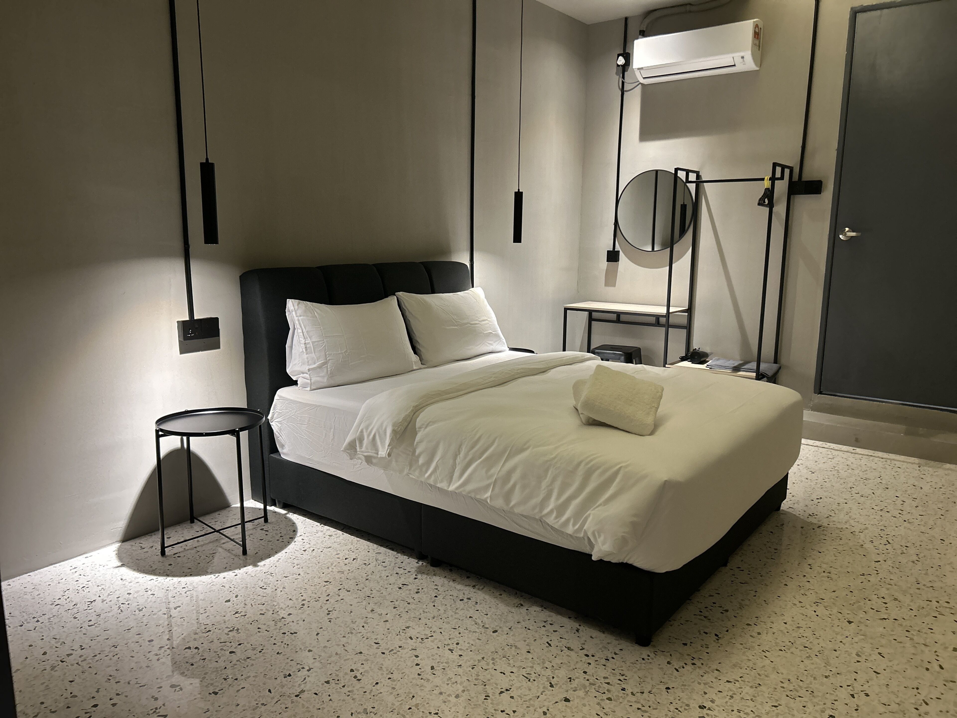Un dormitorio moderno con cabecera negra, ropa de cama blanca, un espejo redondo y una mesita de noche pequeña.
