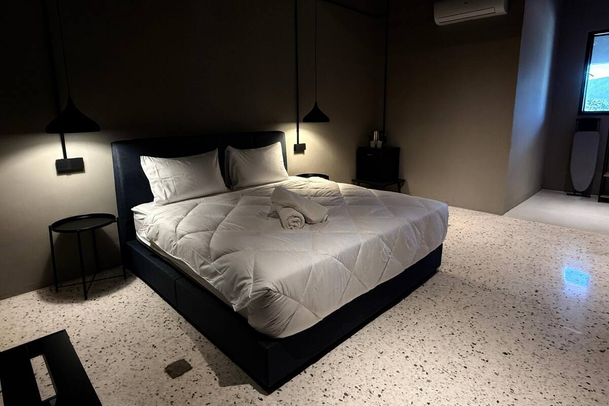 A modern bedroom with a large bed, two bedside tables, a small round table, and an air conditioning unit.