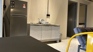 Una cocina moderna con refrigerador empotrado, un lavamanos y una pequeña zona de comedor con una silla amarilla.
