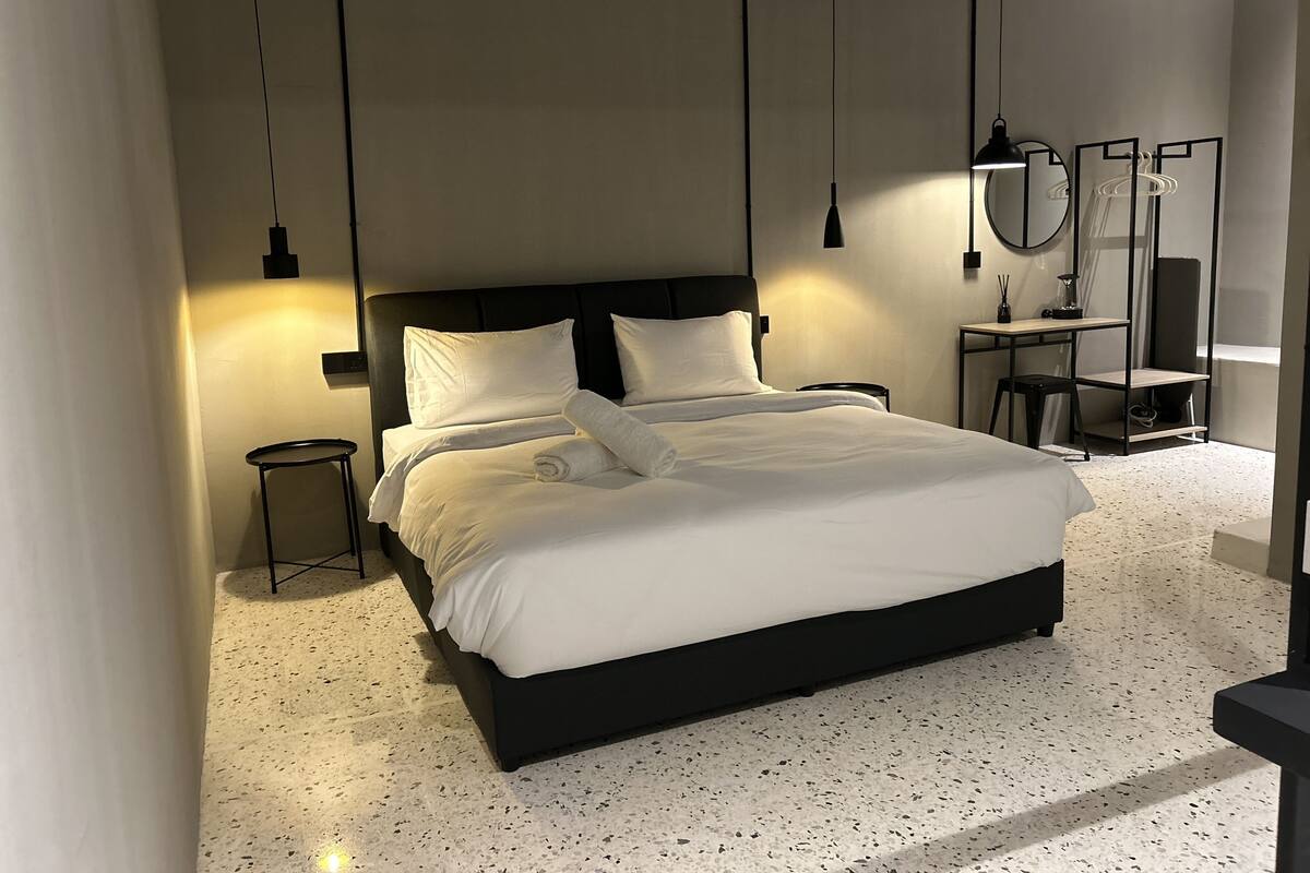A modern bedroom with a large bed, a bedside table, a mirror, and a small stool.