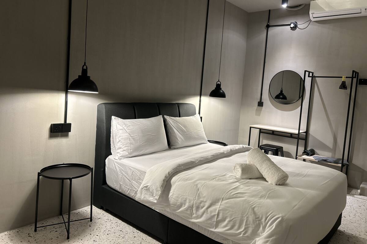 A modern bedroom with a large bed, bedside tables, a round mirror, and pendant lights.